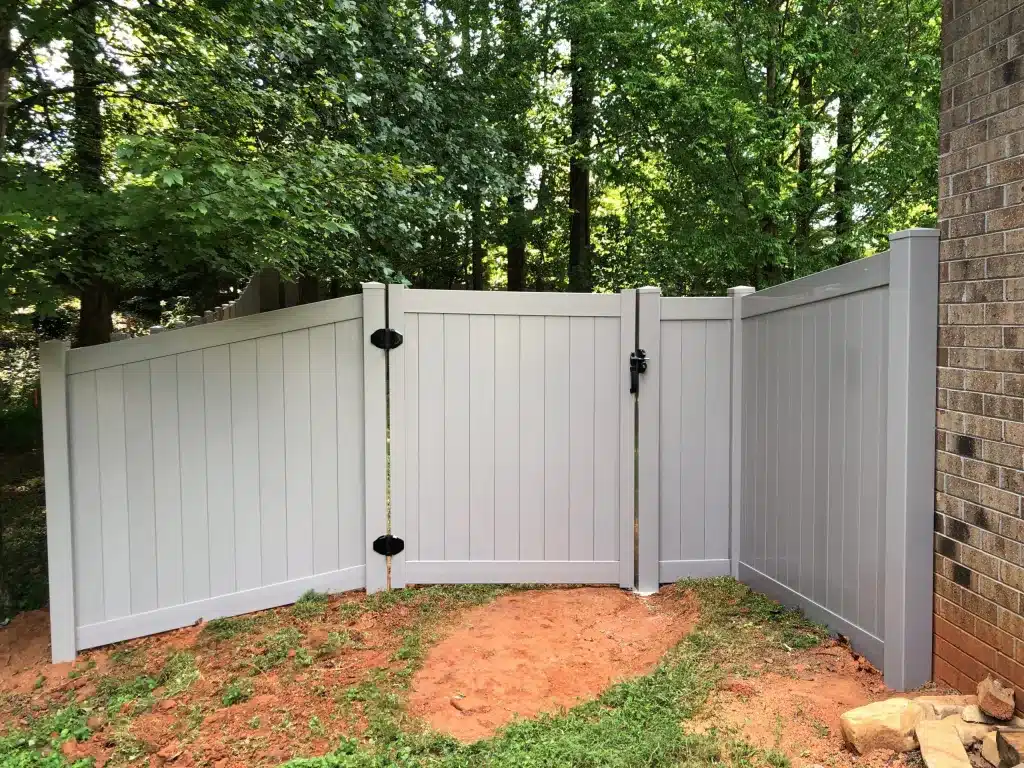 Light gray vinyl privacy fence panels creating corner enclosure near brick home