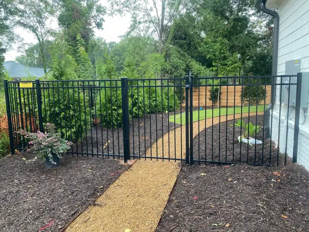 Modern black aluminum fence installed beside a home with fresh mulch and greenery.
