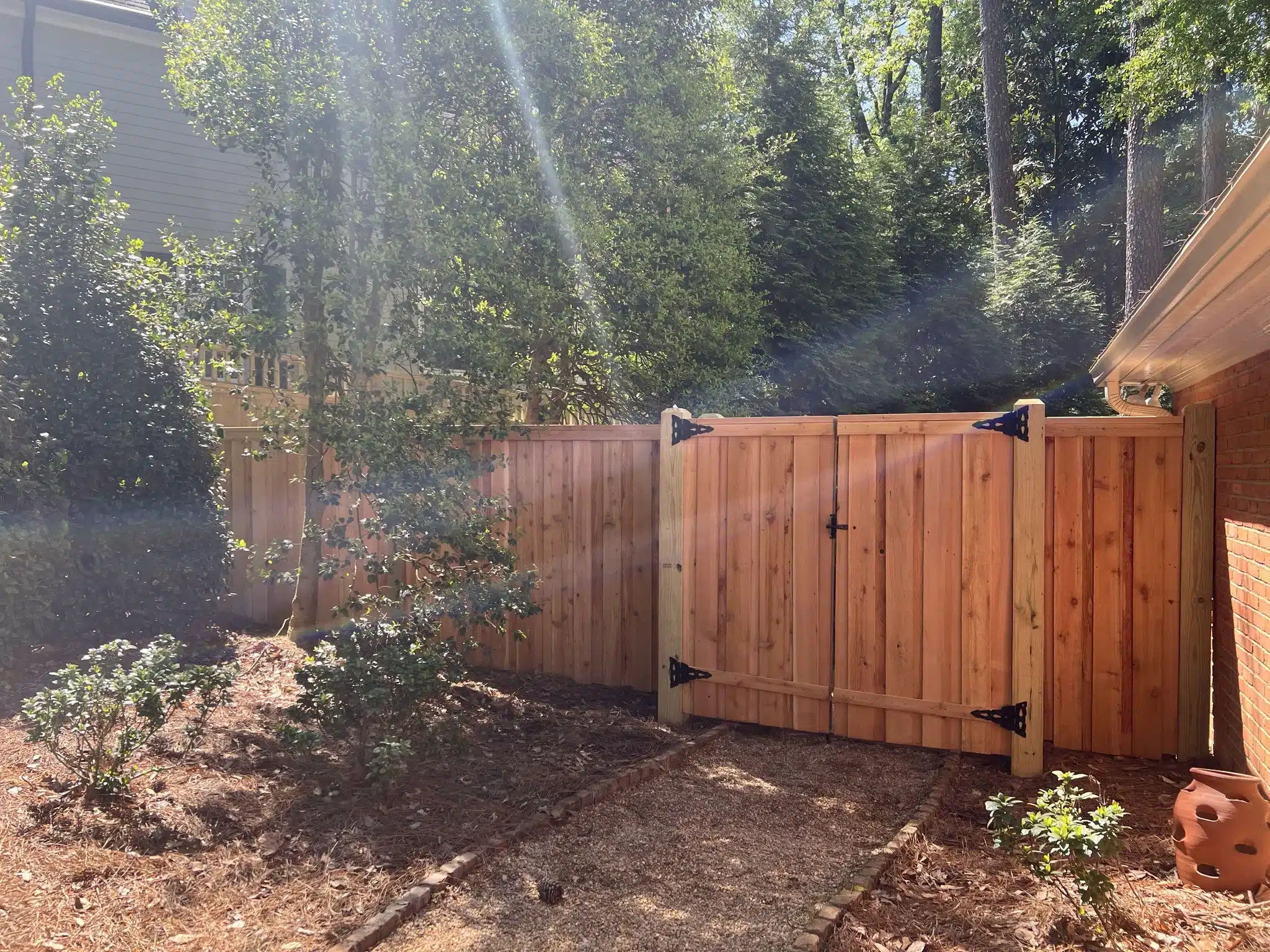 Newly stained vertical wood fence with double gate in a landscaped Atlanta backyard, showcasing even stain application and smooth finish that highlight best practices for staining wood fences to protect and enhance natural beauty.